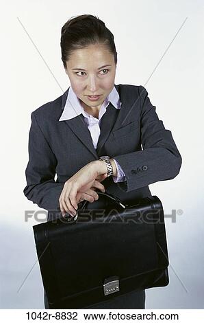 Stock Image - woman, briefcase, Hispanic, watch, business, indoors, anticipating. Fotosearch
