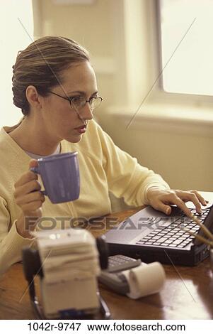 Stock Photo - woman, eyeglasses, computer, laptop, typing, drinking, concentrating. Fotosearch