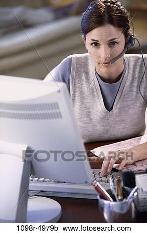 Stock Image - desk, home, woman, headset, computer, phone, typing. Fotosearch