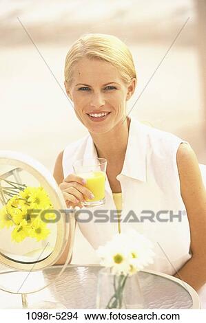 Picture - people, glass, woman, smiling, table, orange juice, drinking. Fotosearch