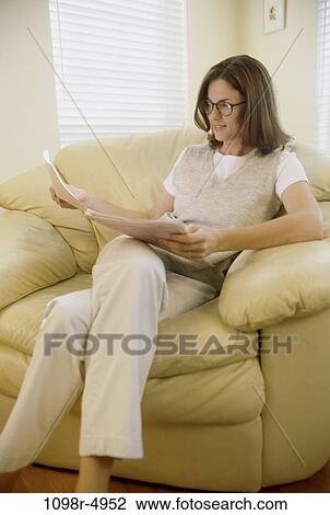 Stock Image - people, woman, eyeglasses, reading, sofa, brunette, indoors. Fotosearch