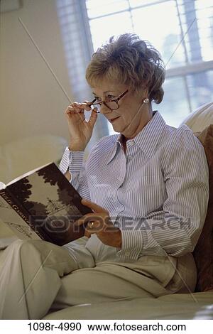 Stock Image - people, woman, eyeglasses, window, senior, reading, book. Fotosearch