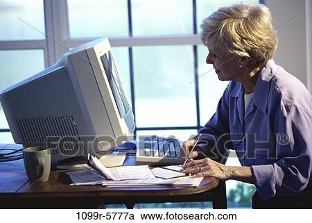 Stock Image - people, woman, senior, computer, writing, finance, bills. Fotosearch
