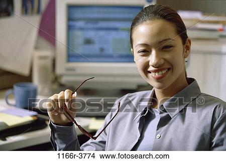 Picture - desk, woman, Asian, eyeglasses, computer, business, casual. Fotosearch