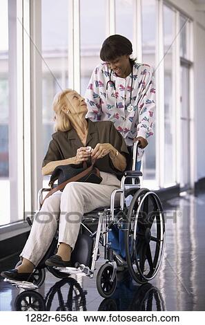 Stock Image - multiethnic, women, patient, wheelchair, nurse, geriatrics, medicine. Fotosearch