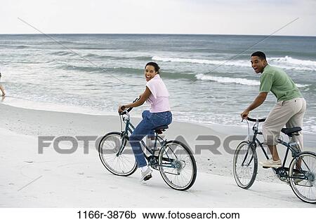 Stock Image - people, couple, beach, riding, bicycles, bike, cycling. Fotosearch