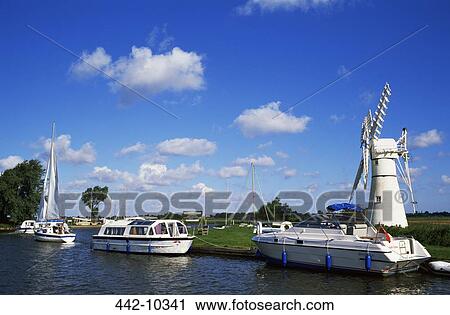 Stock Image - Boats moored near a traditional windmill, River Thurne, Norfolk Broads, Norfolk, England. Fotosearch