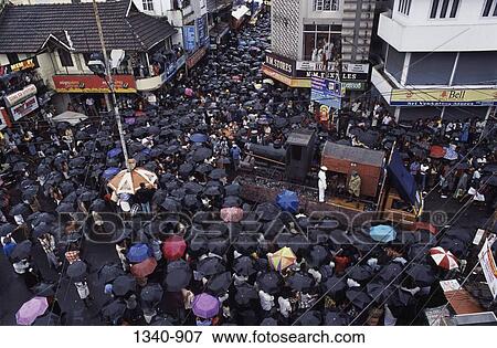 Stock Photo - Crowd sheltering under umbrellas at a town square during rainy season, Kerala, India. Fotosearch