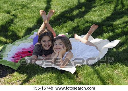 Stock Image - High angle view of two girls lying in grass. Fotosearch