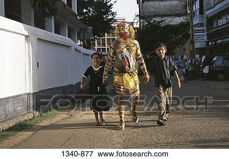 Puli Kali dancer walking with a girl and a boy in a street, Pulikali, Kerala, India View Large Photo Image Stock Photo - Puli Kali dancer walking with a girl and a boy in a street, Pulikali, Kerala, India. Fotosearch