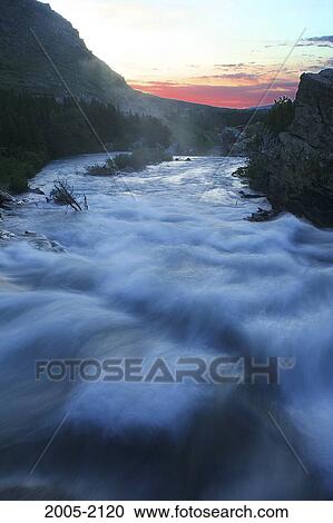 Stock Image - River flowing around rocks at sunrise, Sunrift Gorge, US Glacier National Park, Montana, USA. Fotosearch