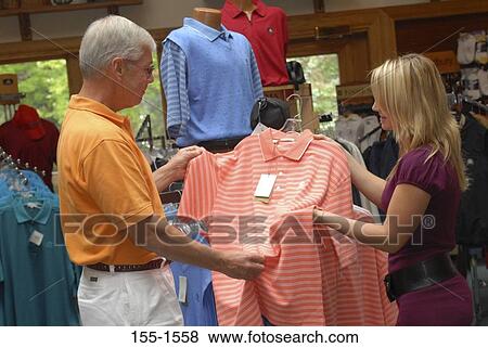 Stock Photo - Side profile of a senior man looking at a polo shirt in a store with his granddaughter. Fotosearch