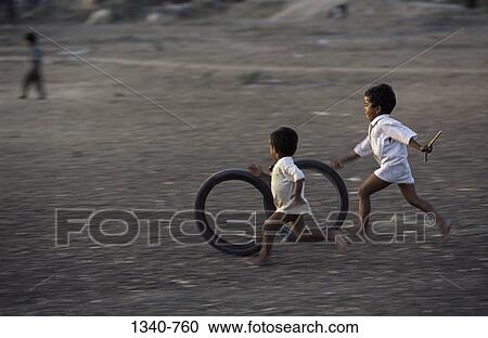 Stock Image - Two boys playing with tires, Tamil Nadu, India. Fotosearch