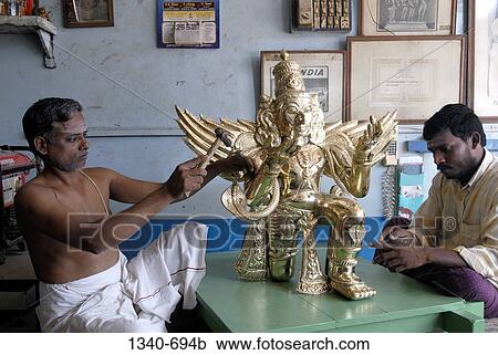 Stock Image - Two sculptors making a bronze sculpture of Garuda the vahana of Lord Vishnu in Hindu mythology, Kumbakonam, Thanjavur District, Tamil Nadu, India. Fotosearch