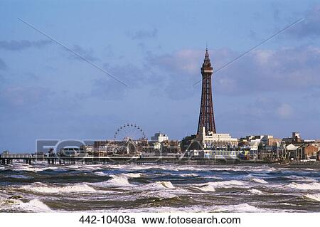 Stock Image - Waves in the sea with a tower and a ferris wheel in the background, Blackpool Tower, Blackpool, Lancashire England. Fotosearch