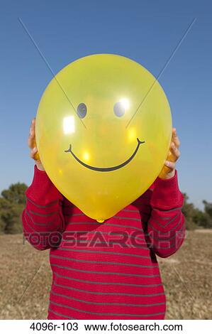 Boy holding a smiley face balloon in front of his face View Large Photo Image Stock Image - Boy holding a smiley face balloon in front of his face. Fotosearch