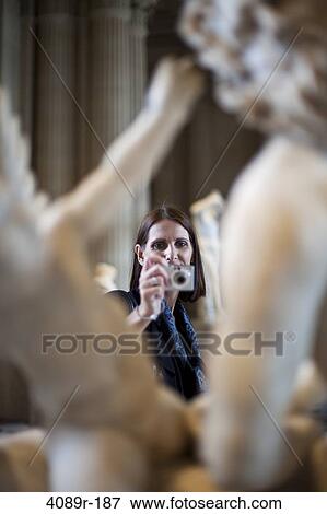 Stock Photo - Mature woman taking a picture of statues in a museum, Paris, France. Fotosearch