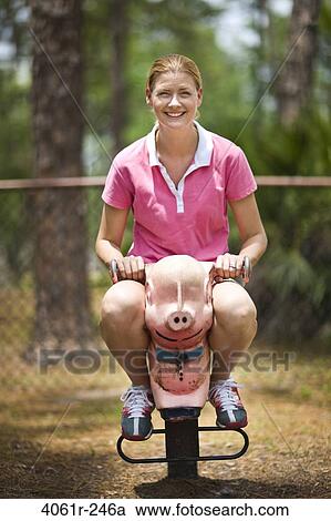 Stock Image - Mid adult woman sitting on a rocking pig. Fotosearch