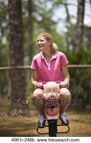 Stock Image - Mid adult woman sitting on a rocking pig. Fotosearch