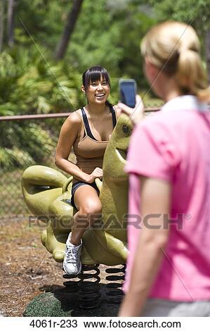 Mid adult woman taking a picture of her friend on a rocking dinosaur View Large Photo Image Stock Image - Mid adult woman taking a picture of her friend on a rocking dinosaur. Fotosearch