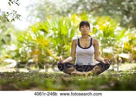Stock Image - Young woman practicing yoga in a park. Fotosearch