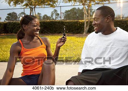 Stock Image - Young woman taking a picture of her boyfriend with a mobile phone. Fotosearch