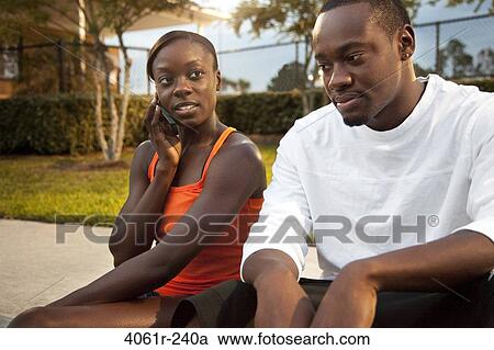 Stock Image - Young woman talking on a mobile phone beside her boyfriend. Fotosearch