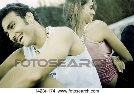 Close-up of a young couple sitting back to back View Large Photo Image Picture - Close-up of a young couple sitting back to back. Fotosearch