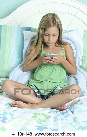 Girl sitting on the bed and text messaging on a mobile phone View Large Photo Image Stock Photo - Girl sitting on the bed and text messaging on a mobile phone. Fotosearch