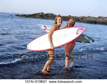 Stock Photo - Portrait of two young women carrying surfboards on the beach. Fotosearch