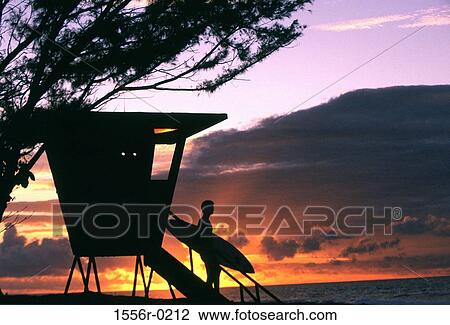 Stock Image - Silhouette of surfer by beach hut, Hawaii, USA. Fotosearch