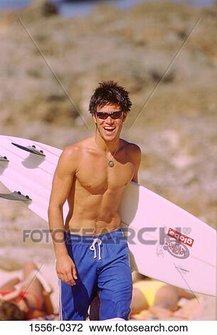 Stock Image - Teenage boy carrying surfboard. Fotosearch