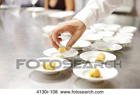 Stock Photo - USA, New York City, Brooklyn, close up of chef's hand putting appetizers on plates. Fotosearch