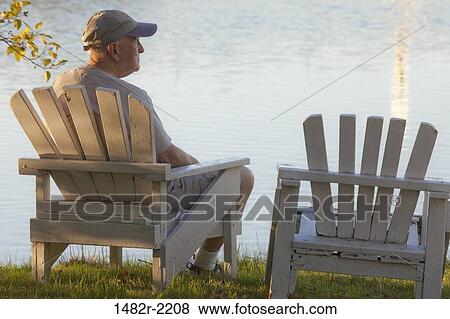 Stock Photo - USA, Washington, Seabeck, Seabeck Conference Center, senior man sitting on deck chair and looking at river. Fotosearch