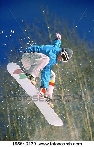 Stock Image - Young adult man performing stunt on snowboard. Fotosearch