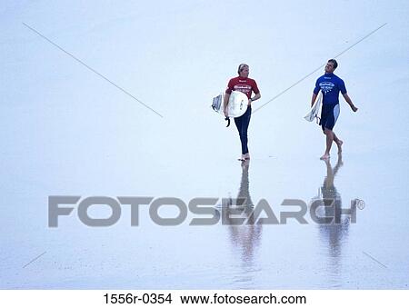 Young men walking along beach carrying surfboards View Large Photo Image Picture - Young men walking along beach carrying surfboards. Fotosearch