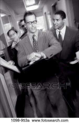 Stock Image - multiethnic, time, coworkers, paperwork, papers, watch, hallway. Fotosearch