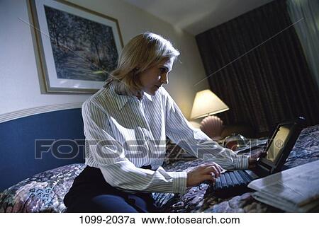 Stock Image - hotel, woman, newspaper, lamp, laptop, bed, business. Fotosearch
