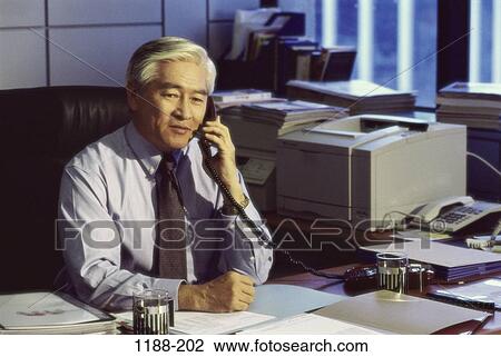 Stock Image - desk, telephone, paperwork, Asian, listening. Fotosearch