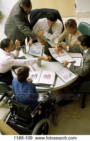 Stock Photo - multiethnic, groups, table, charts, wheelchair, pointing, business. Fotosearch