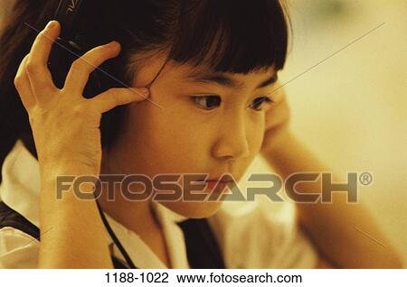 Stock Image - people, headset, Asian, listening, girl, concentrating. Fotosearch
