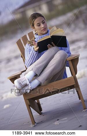 Stock Image - people, woman, chair, reading, beach, book, sweater. Fotosearch
