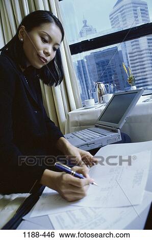 Stock Photograph - woman, paperwork, Asian, computer, laptop, business, writing. Fotosearch