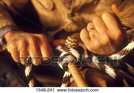 Stock Image - Cowboy's hands braiding leather for a bridle and bit. Fotosearch