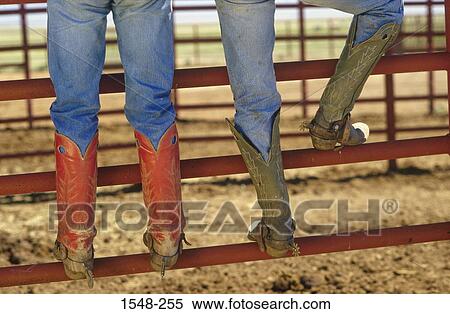 Stock Photography - Low section view of two cowboys standing on a fence. Fotosearch
