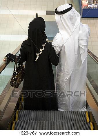 Rear view of a couple standing on an escalator in a shopping mall, Dubai, United Arab Emirates View Large Photo Image Stock Photo - Rear view of a couple standing on an escalator in a shopping mall, Dubai, United Arab Emirates. Fotosearch