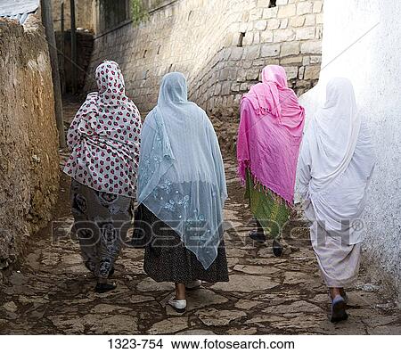 Picture - Rear view of four women walking together on a street, Harar, Ethiopia. Fotosearch