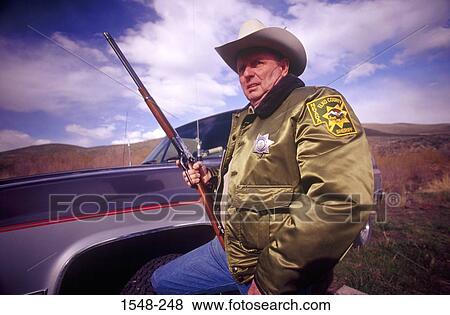 Stock Photo - Sheriff holding a rifle and standing beside a truck. Fotosearch