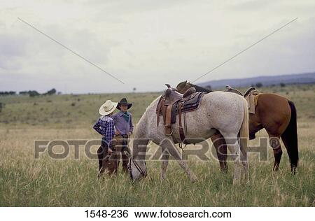 Two cowboys standing with their horses grazing in a field, New Mexico, USA View Large Photo Image Stock Photograph - Two cowboys standing with their horses grazing in a field, New Mexico, USA. Fotosearch