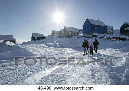 Stock Image - Four people walking on a snow covered road, Ammassalik, Greenland. Fotosearch